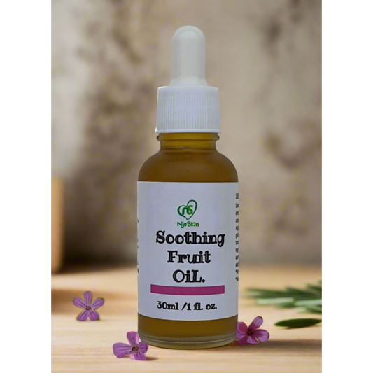 A bottle of Soothing Fruit Oil with a dropper, labeled with the product name and capacity, placed on a wooden surface with flowers around it.